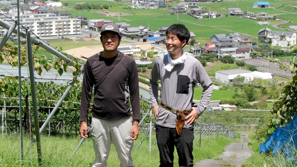 キウイ畑の前に立つ深山のキウイのおふたり